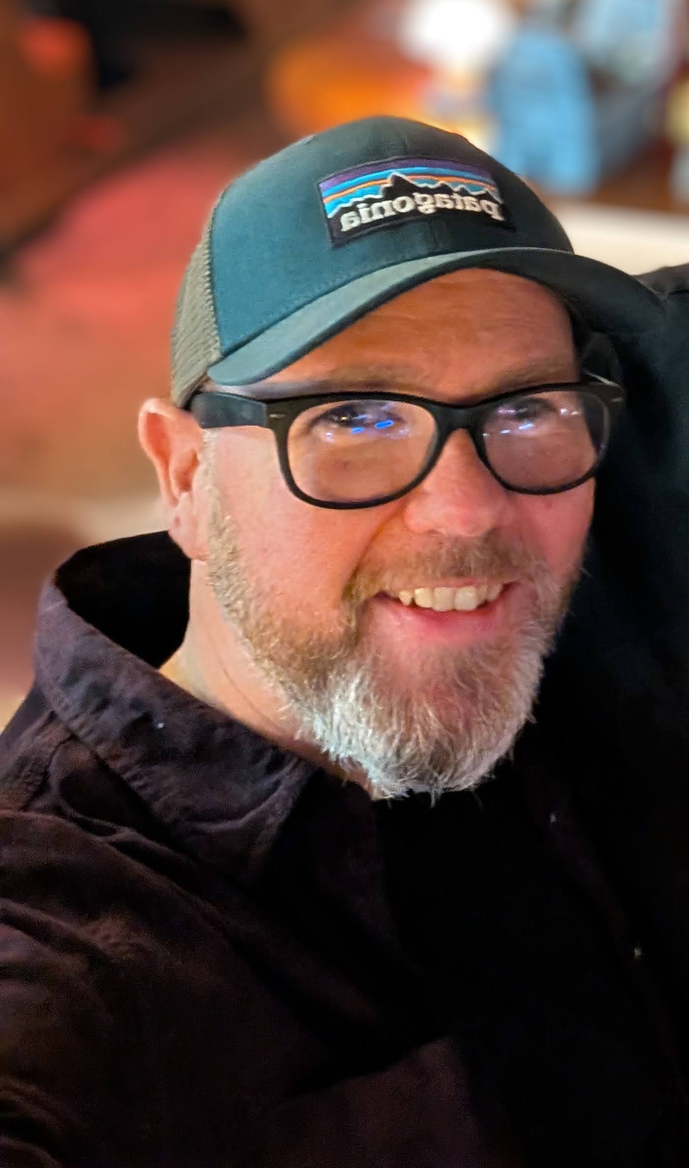 Andrew Smith, smiling, wearing a green Patagonia cap and dark-framed glasses.